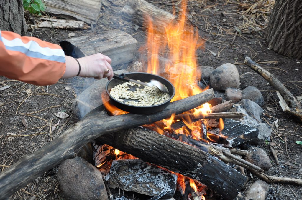 A roaring fire heats a cast iron of roasting pumpkin seeds.